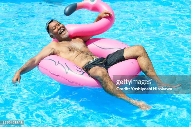 senior man floating on rooftop pool with inflatable pool toy - summer comedies party stockfoto's en -beelden