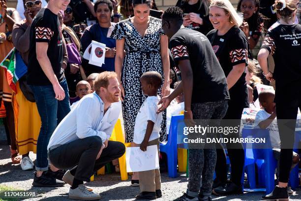 Boy offers a gift to Prince Harry, Duke of Sussex and Meghan, Duchess of Sussex as they arrive to visit the "Justice desk", an NGO in the township of...