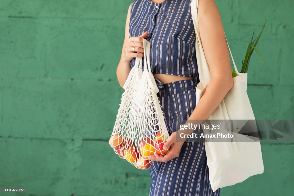 Weibliche Hände mit Einkaufen Baumwolle Mesh Eco Tasche auf grünem Hintergrund. Null-Abfall-Konzept