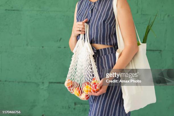 mains femelles avec le sac écologique de maille de coton d'achat sur le fond vert. concept zéro déchet - vegetable stock photos et images de collection