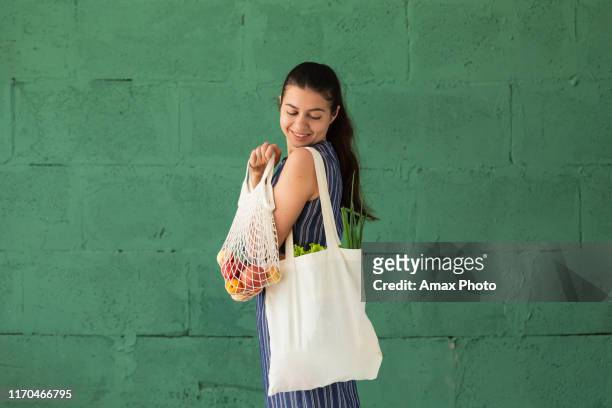 vrouw winkelen groenten en fruit met herbruikbare katoen eco producten tas. zero waste lifestyle concept - tas stockfoto's en -beelden