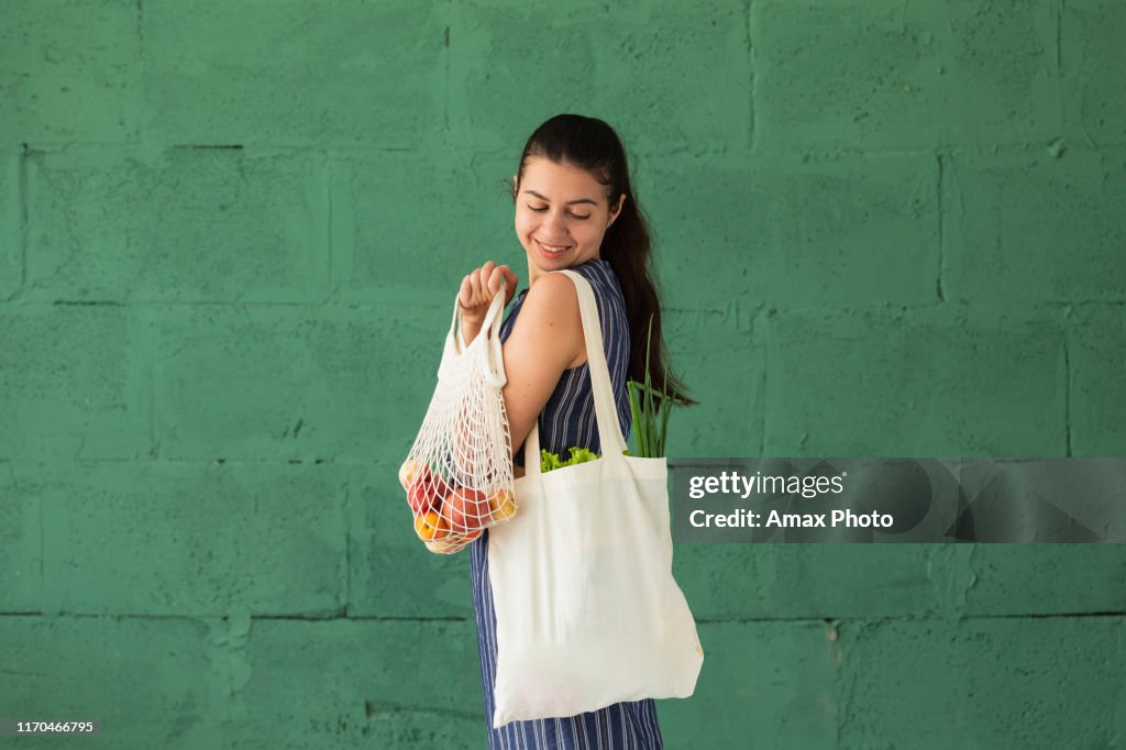 Woman shopping fruits and vegetables with reusable cotton Eco produce bag. Zero waste lifestyle concept