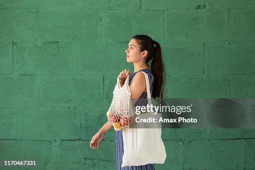 Young woman with shopping cotton Eco bag with fruits and vegetables in her hands on green wall background. Lifestyle, zero waste concept Young woman with shopping cotton Eco bag with fruits and vegetables in her hands on green wall background. Lifestyle, zero waste concept