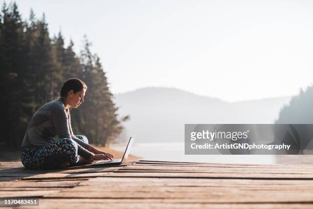 woman using laptop outdoor at wooden pier. - remote location stock pictures, royalty-free photos & images