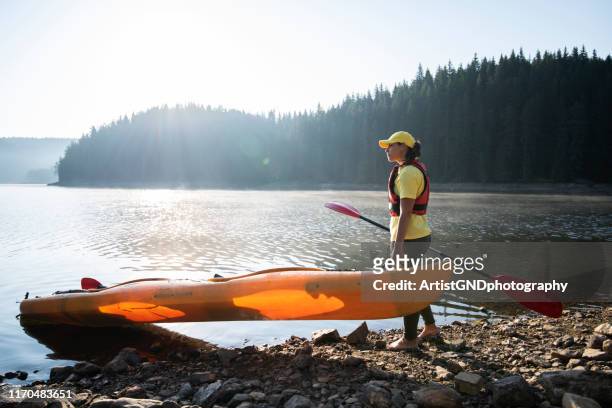 a woman preparing to kayaking in mountain lake. - carrying kayak stock pictures, royalty-free photos & images