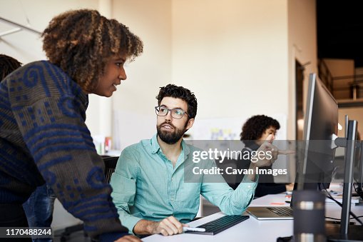 Businessman explaining to businesswoman over desktop computer at desk in office Businessman explaining to businesswoman over desktop computer at desk in office