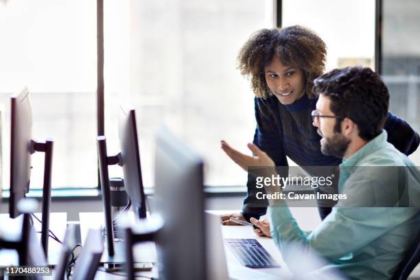 business people discussing over desktop computer at desk against window in office - standing at attention stock pictures, royalty-free photos & images