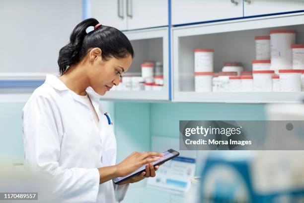 young pharmacist using digital tablet in hospital - female pharmacist with a digital tablet imagens e fotografias de stock