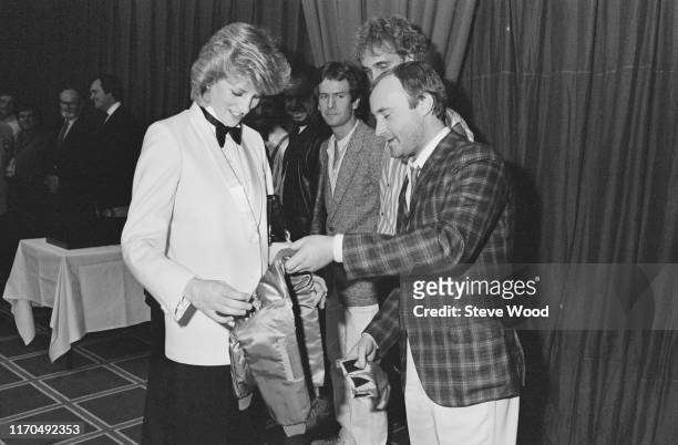 Diana, Princess of Wales accepts a jacket with an embroidered gold crown for Prince William from British singer and drummer Phil Collins of rock band...