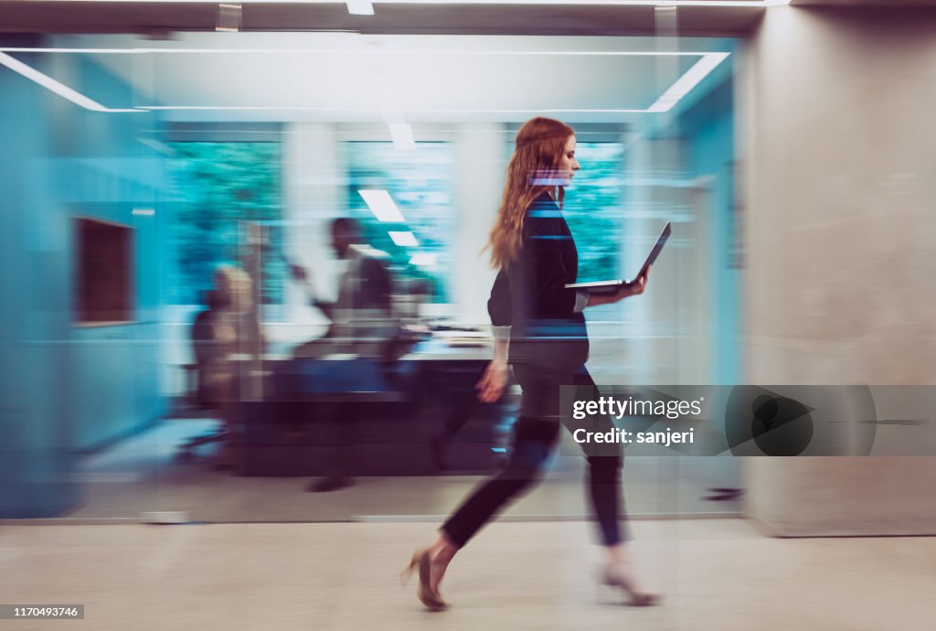 Mujer de negocios sosteniendo un ordenador portátil, caminando por el pasillo