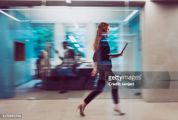 mujer de negocios sosteniendo un ordenador portátil, caminando por el pasillo - esfuerzo fotografías e imágenes de stock