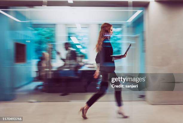 femme d'affaires retenant un ordinateur portatif, marchant en bas du couloir - être en mouvement photos et images de collection