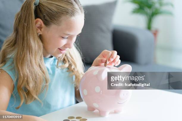 achtjähriges mädchen legt münzen in ihr sparschwein. drinnen geschossen. - 8 9 years stock-fotos und bilder