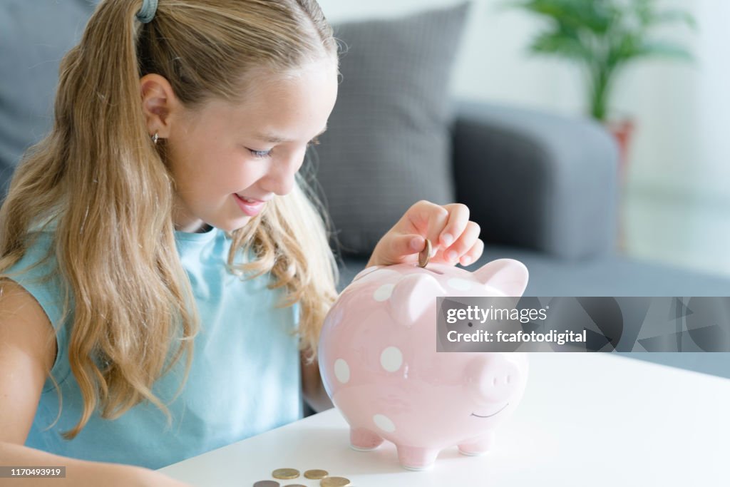Eight years old girl placing coins in her piggy bank. Indoors shot.