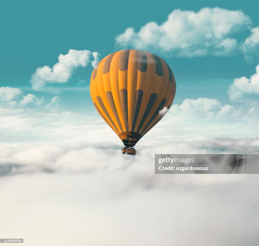 Yellow hot air balloon flying above the clouds