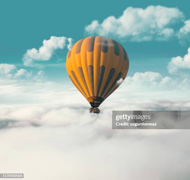 yellow hot air balloon flying above the clouds - blowing balloon stock pictures, royalty-free photos & images