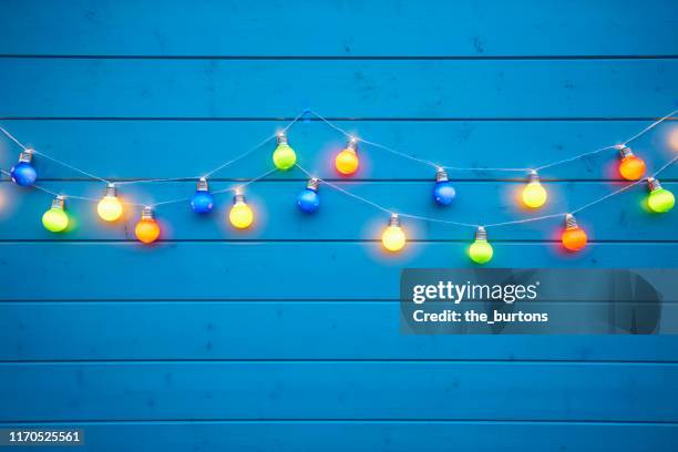 colorful string lights for party decoration at a blue painted wooden wall - cadena de luces fotografías e imágenes de stock