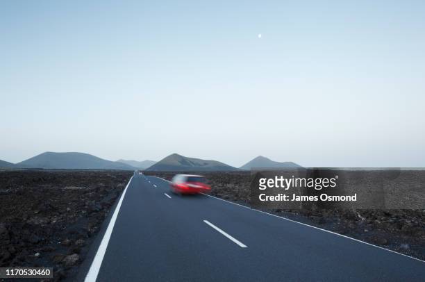 red car in blurred motion travelling on straight road crossing lava plains towards distant volcanoes. - rijden een motorvoertuig besturen stockfoto's en -beelden