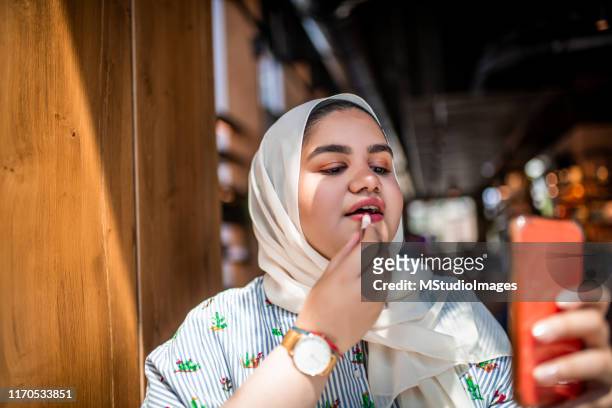 muslim girl putting on a red lipstick - chubby arab stock pictures, royalty-free photos & images