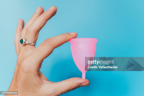 woman holding a pink menstrual cup on blue background - period cup stock-fotos und bilder