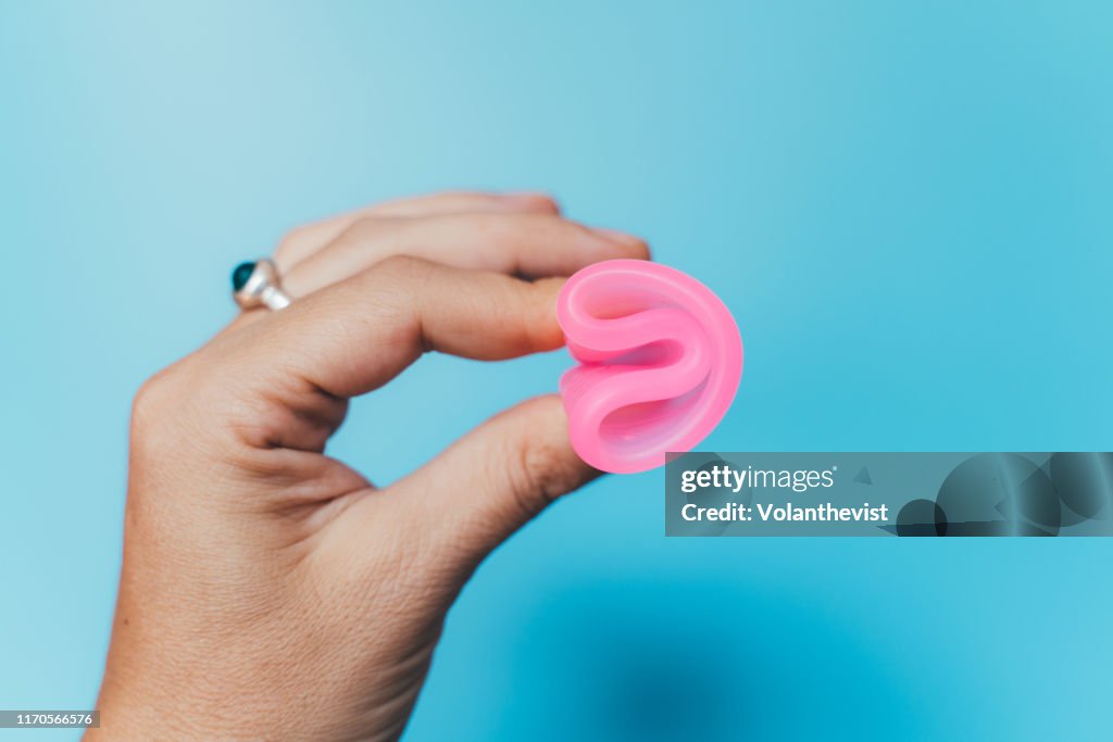 Woman holding a pink menstrual cup on blue background