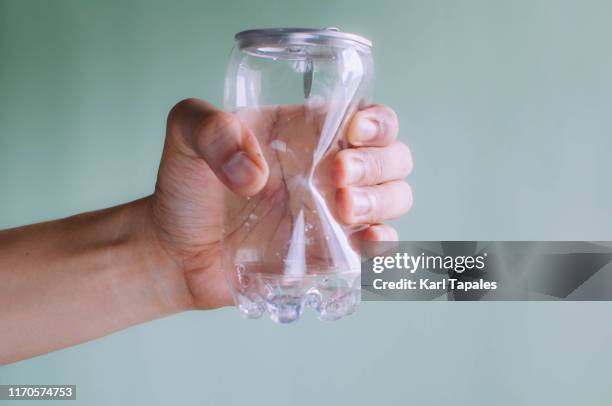 a young person is holding a crumpled plastic and tin soda can on a green background - estaño fotografías e imágenes de stock