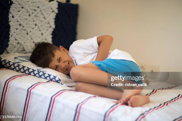 joven acostado en la cama con dolor de estómago - one boy only fotografías e imágenes de stock