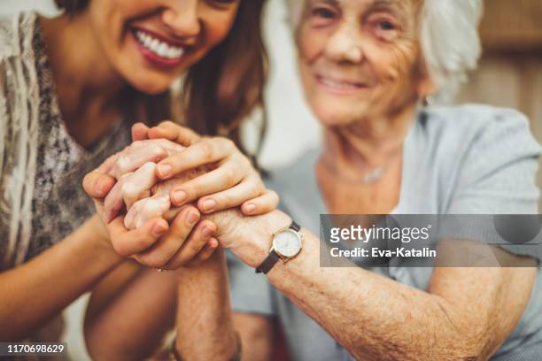 plan rapproché d'une infirmière de sourire retenant la main d'une femme aînée - souvenirs photos et images de collection