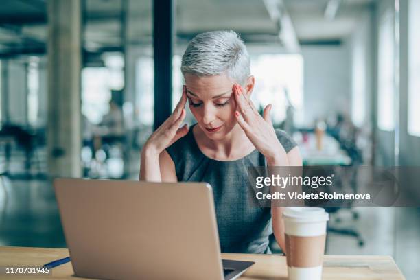 female entrepreneur with headache sitting at desk - frustrated business person stock pictures, royalty-free photos & images