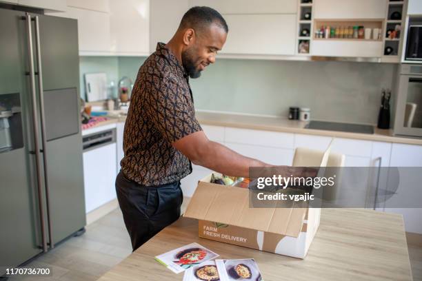 latin man opening parcel with meal kit - meal kit stock pictures, royalty-free photos & images