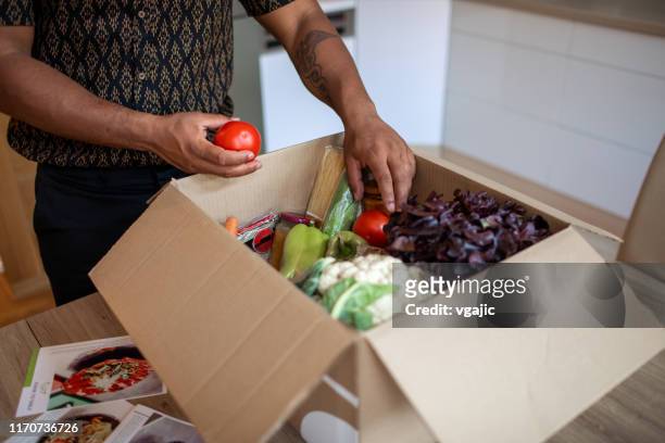 latin man opening parcel with meal kit - meal stock pictures, royalty-free photos & images