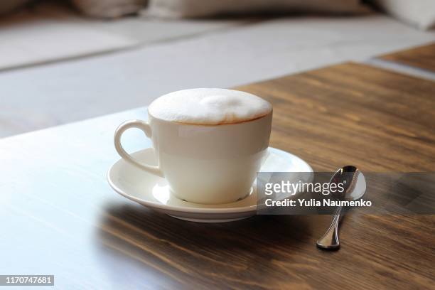 cup of cappuccino on a wooden table in a cafe. beautiful foam, white ceramic cup, copy space. - capuccino fotografías e imágenes de stock