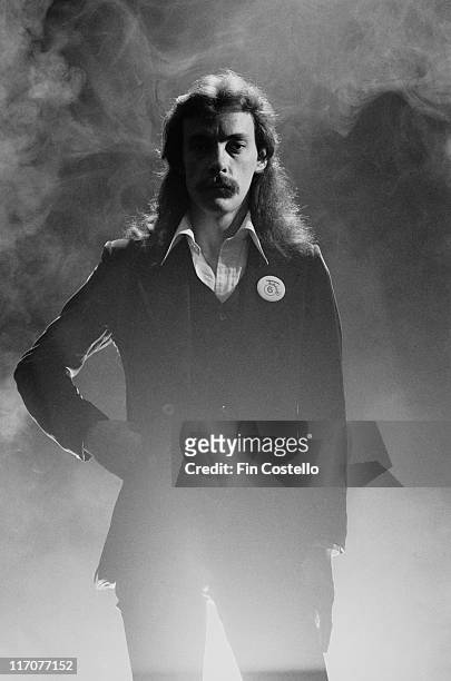 Neil Peart, drummer with Canadian rock band Rush, poses with one hand on his hip, with a smoke behind him in a studio portrait, 1978.