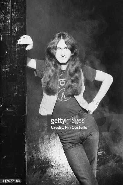 Geddy Lee, singer and bassist with Canadian rock band Rush, poses with one arm leaning on the wall beside him, the other hand resting on his hip, in...