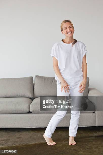 woman in white standing in apartment, smiling - donne bionde scalze foto e immagini stock
