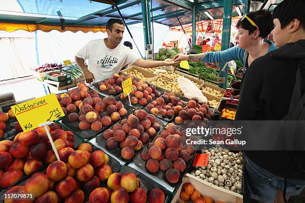 Signs show the prices in Euros while a customer makes a purchase at a fruit and vegetable stand at the Maybacher Ufer outdoor market in Kreuzberg...