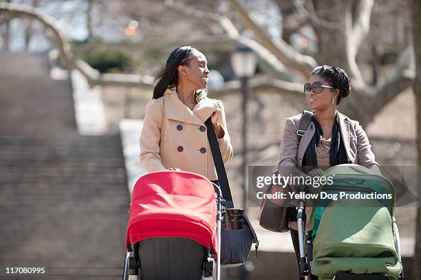 two moms pushing babies in strollers in the park - mother stroller stock pictures, royalty-free photos & images