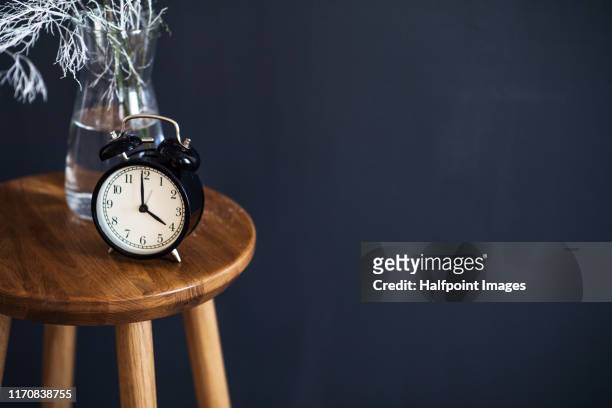a clock and decoration in vase on wooden stool against black background. - glass vase black background foto e immagini stock