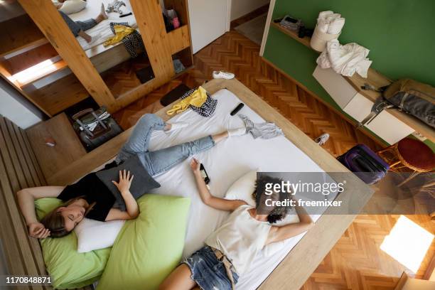two drunk woman sleeping on bed with bottle of whiskey - messy house after party stock pictures, royalty-free photos & images