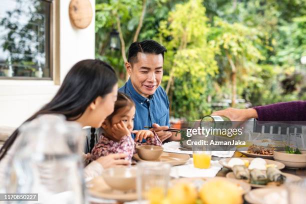 chinese husband and wife guiding young daughter at lunch - chinese family eating stock pictures, royalty-free photos & images