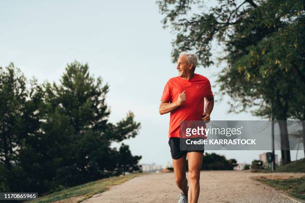 senior retired man runs and performs exercise - correr imagens e fotografias de stock