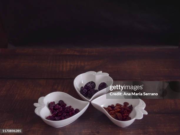 autumn fruits: groups of dried cranberry, prunes and raisins in heart-shaped porcelain bowls on an old wooden table - cranberry heart stock-fotos und bilder