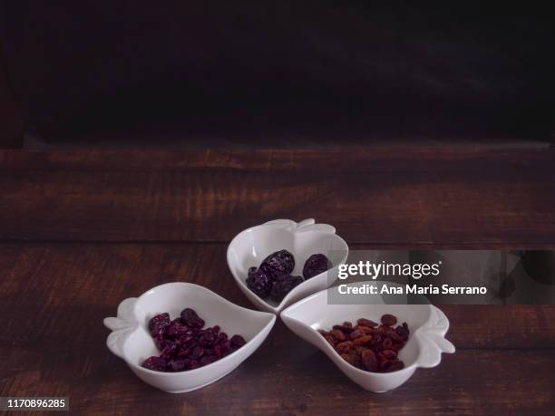 autumn fruits: groups of dried cranberry, prunes and raisins in heart-shaped porcelain bowls on an old wooden table - cranberry heart stock pictures, royalty-free photos & images