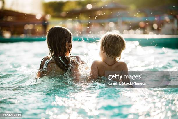 vista posteriore bambino e ragazza seduti e schizzi in piscina - child swimming foto e immagini stock