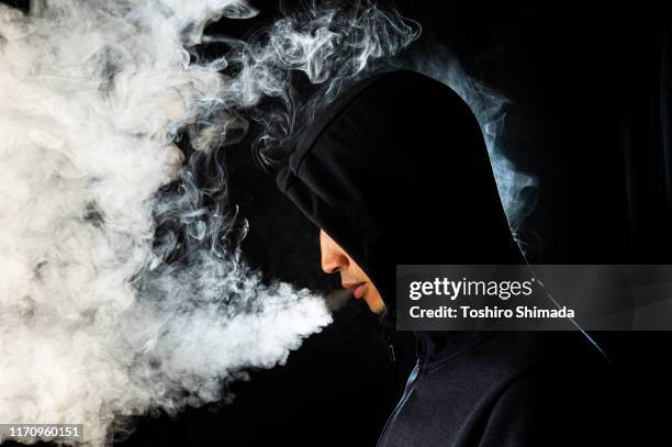 a hoody man smoking vape and exhaling - electronic cigarette smoke stockfoto's en -beelden