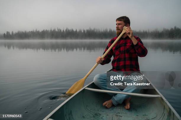 man paddling a canoe in montana on a foggy lake - röda byxor bildbanksfoton och bilder