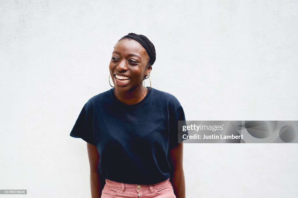 Confident woman laughing and looking off camera shot against white wall