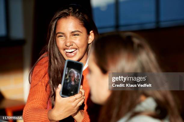 woman showing photograph on mobile phone to friend - school photo stockfoto's en -beelden