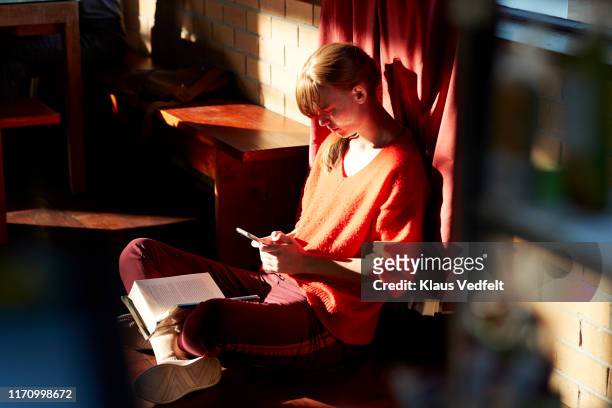 woman using smart phone at cafeteria during break - fashion woman floor cross legged stock pictures, royalty-free photos & images