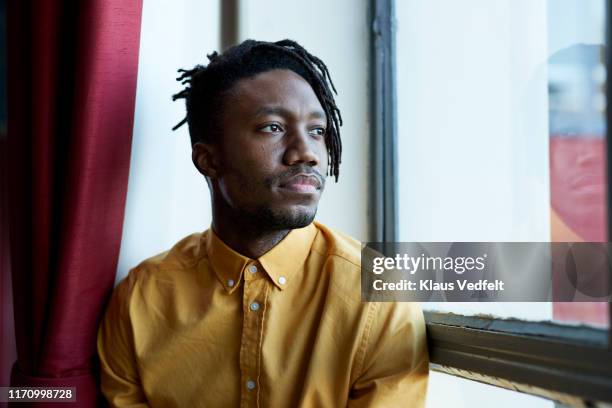 thoughtful young man looking through window - introspection foto e immagini stock